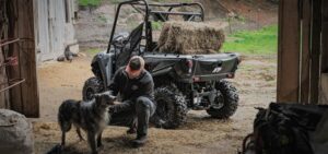 Rear view of an Argo XF 500 carrying a hay bale, with a man and dog in the foreground