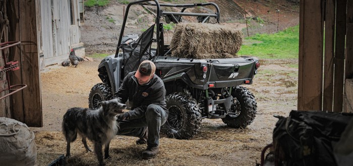 Rear view of an Argo XF 500 carrying a hay bale, with a man and dog in the foreground